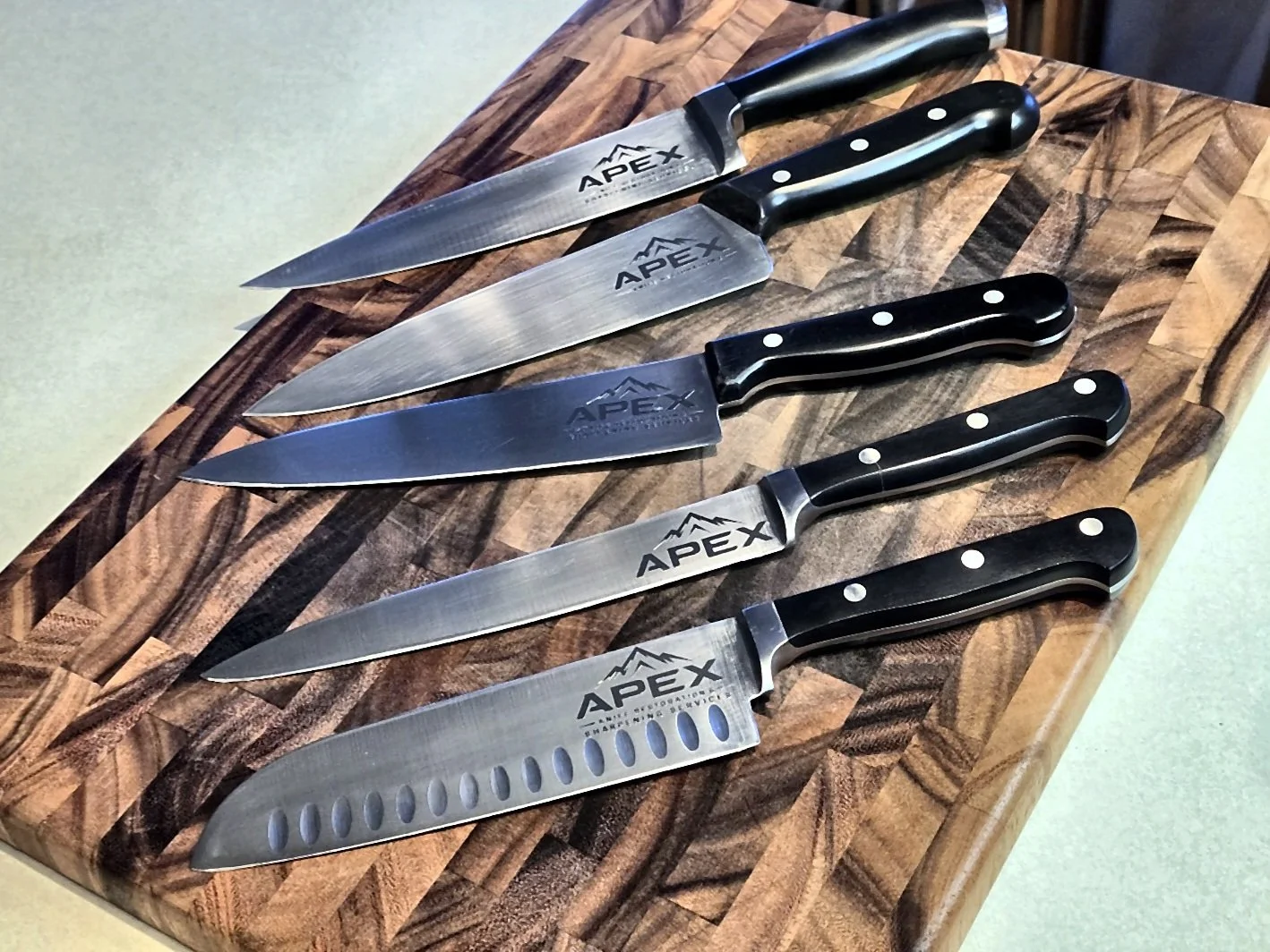 Apex-branded kitchen knives arranged on a wooden cutting board.