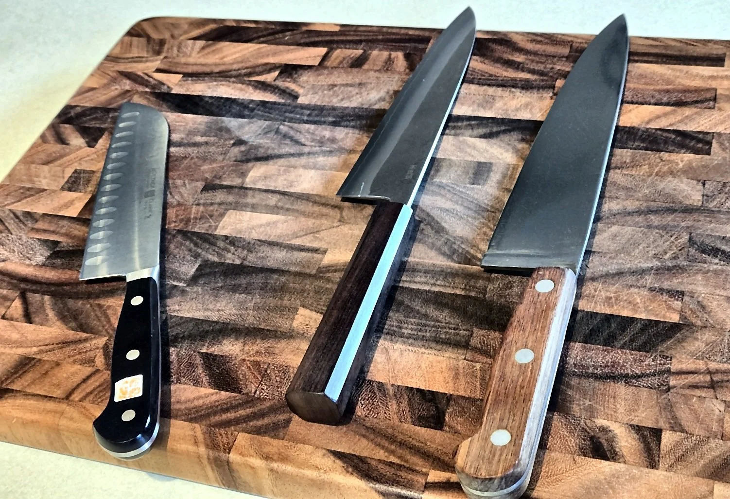 Three finished kitchen knives arranged on a wooden cutting board.