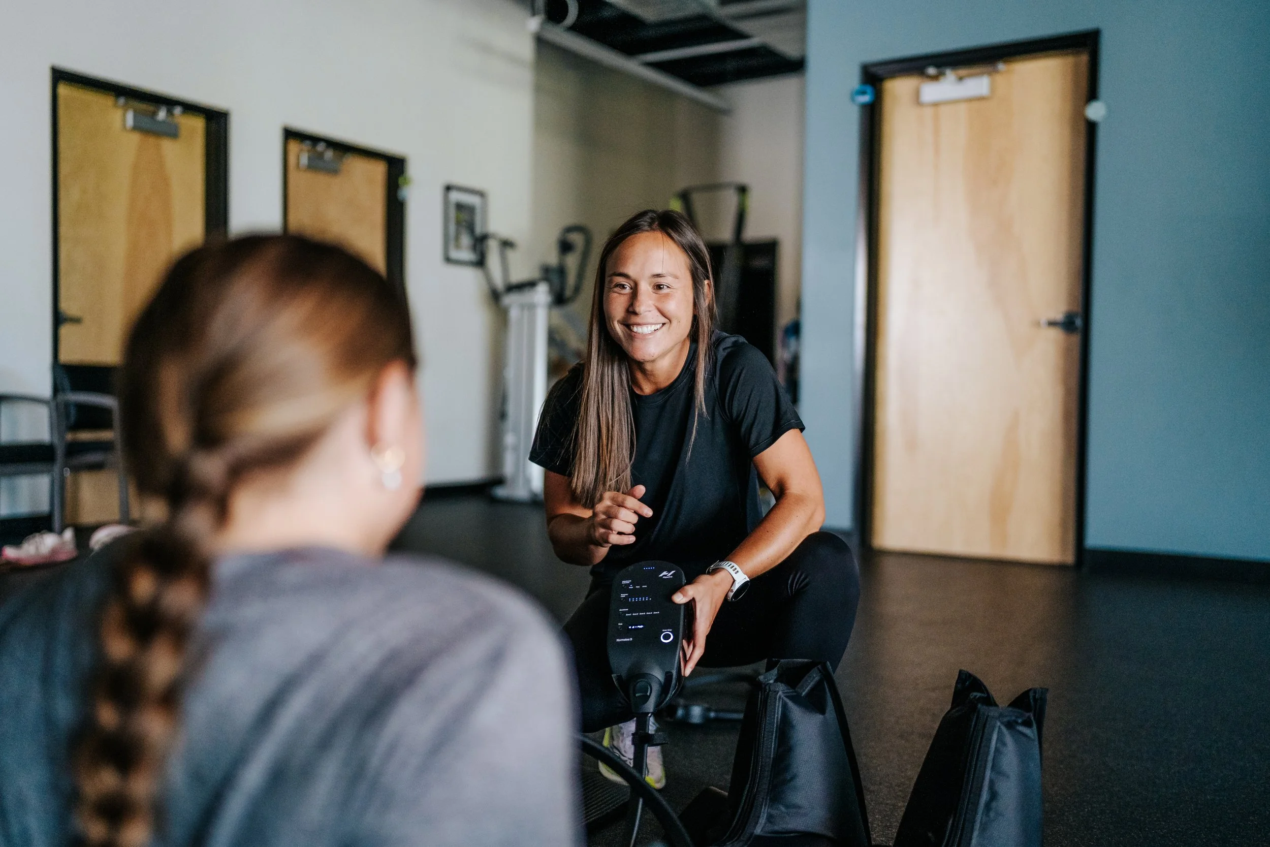 Breaking Lines founder Ali Ohashi kneels beside a young female athlete, helping her use Hyperice compression recovery equipment during a training session in Boise, Idaho.