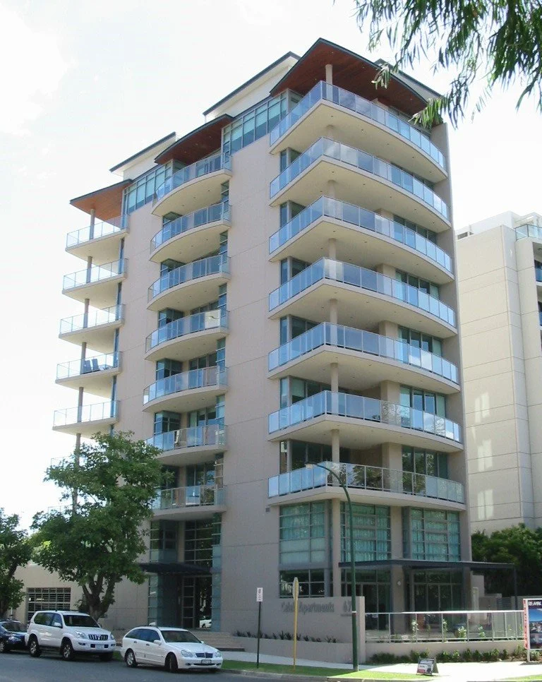 Modern multi-story residential building with curved balconies, glass railings, and large windows.