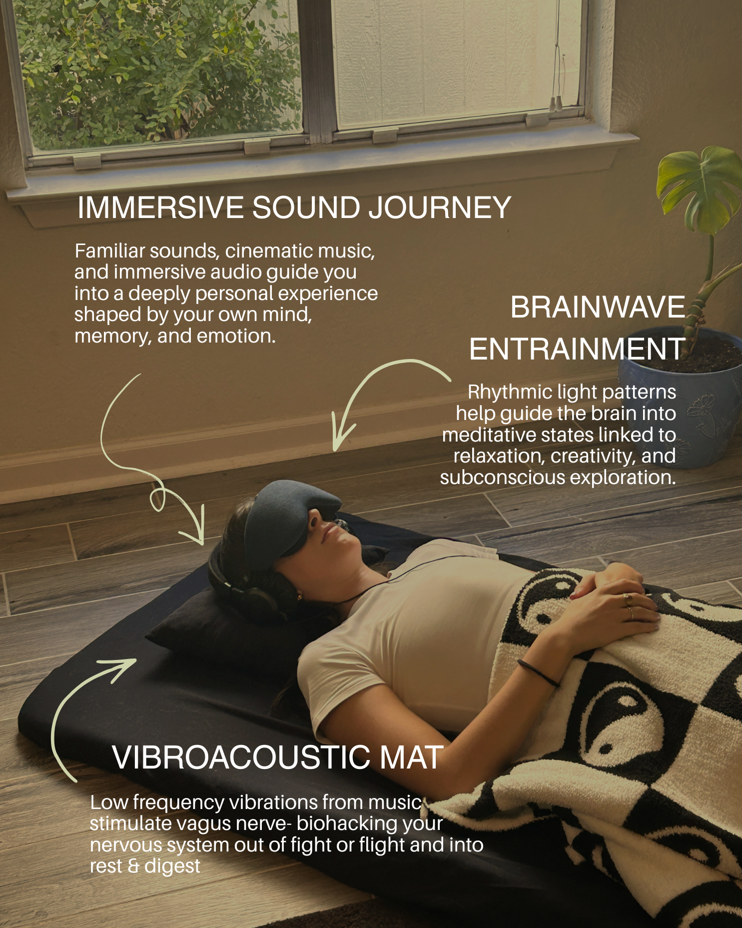 A woman lies on a black vibroacoustic mat with a blanket over her legs, wearing headphones and a sleep mask, in a room with a large window and a potted plant nearby, demonstrating immersive sound journey, brainwave entrainment, and vibroacoustic therapy.