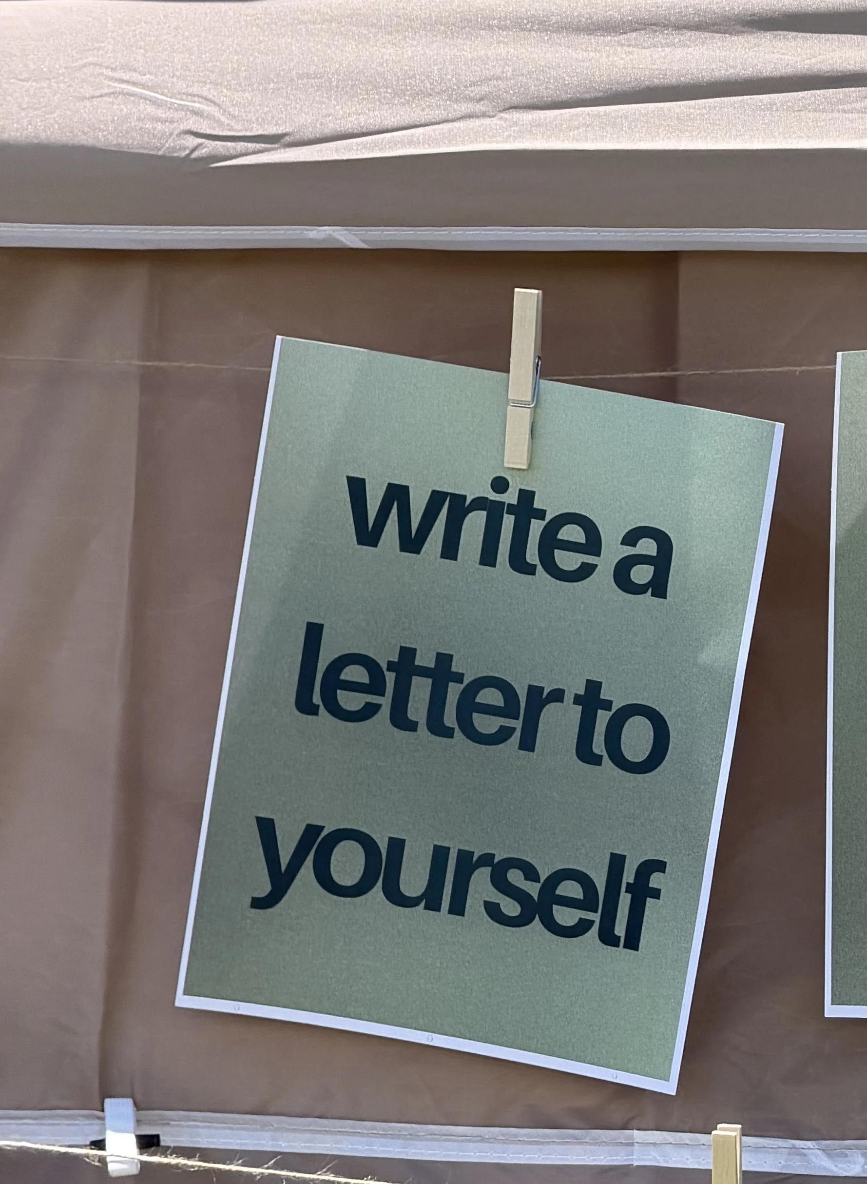 A close-up of a paper sign clipped to a string, with part of the word 'write' visible, on an indoor wall with brown paper and a fabric-covered surface above.