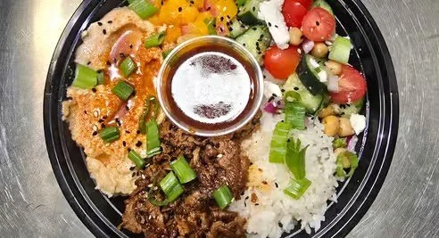 Assorted Mexican food dish with rice, ground beef, cheese, vegetables, and salsa in a black bowl.