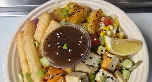 Assorted Mexican food platter with fried taquitos, grilled vegetables, lime wedge, and a cup of dark dipping sauce.