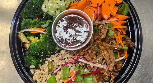 Assorted vegetables, rice, sliced beef, and dipping sauce in a black bowl.