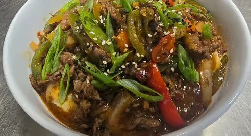 Bowl of stir-fried beef with green onions, red bell peppers, and sesame seeds