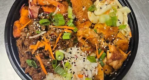 Bowl of rice topped with ground beef, shredded carrots, chopped green onions, sesame seeds, sliced chicken, and chopped lettuce.