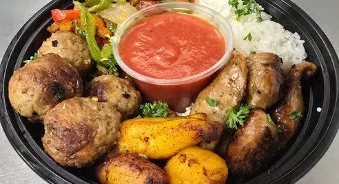 A black meal container with rice, grilled chicken, meatballs, grilled vegetables, roasted potatoes, and a side of red sauce.