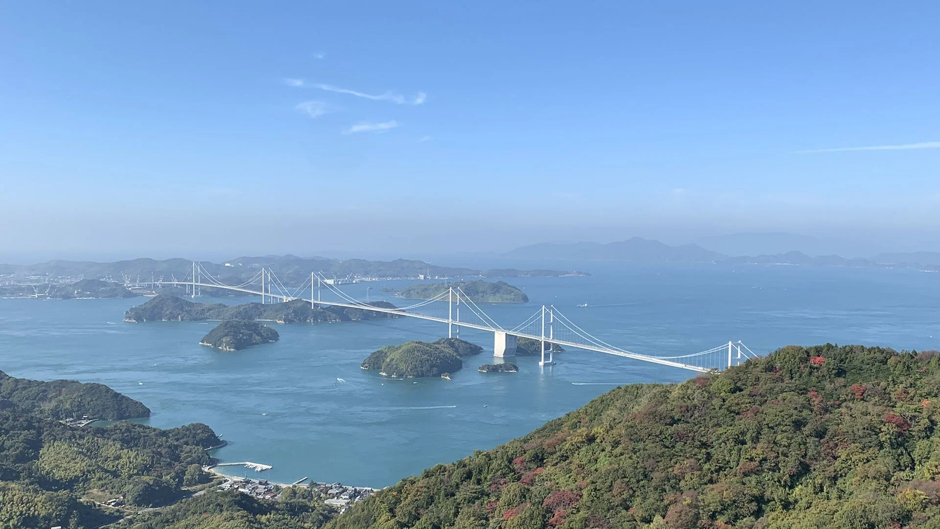 しまなみ海道と島々を望む景色。青空の下、緑豊かな山々と穏やかな海が広がる風景