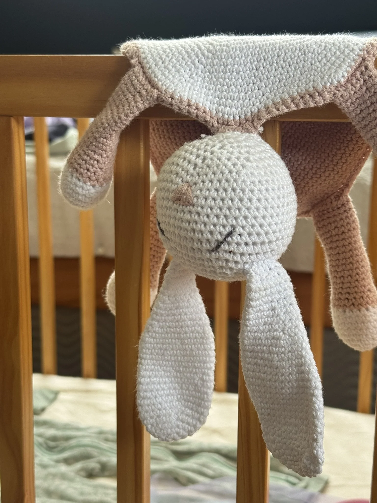 A crochet bunny toy draped over the side of a cot.