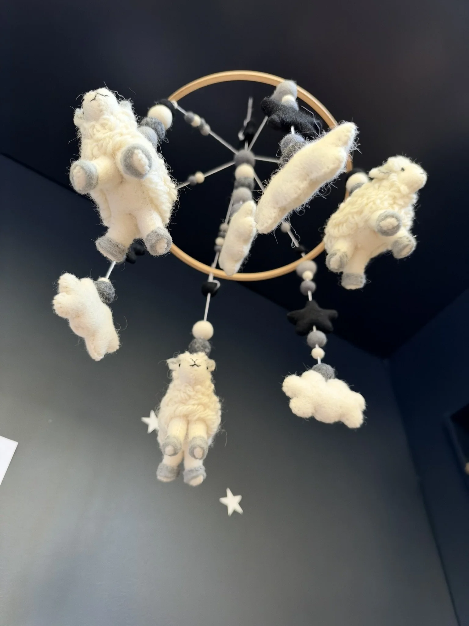 A plush dreamcatcher with white and black felt sheep, stars, and circular elements hanging from a round wooden hoop.