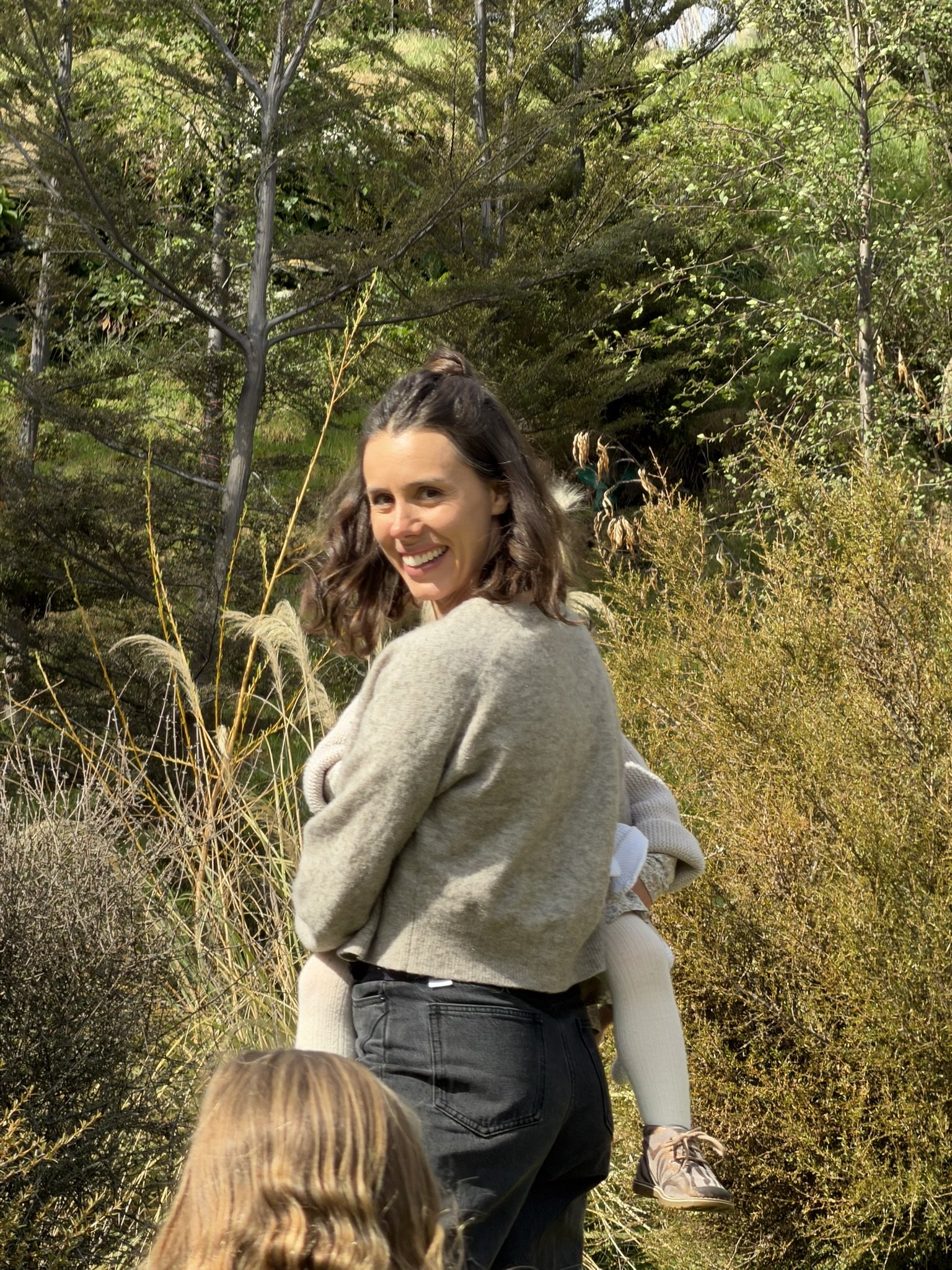 Georgie a Queenstown sleep consultant, smiling at the camera while carrying her daughter.