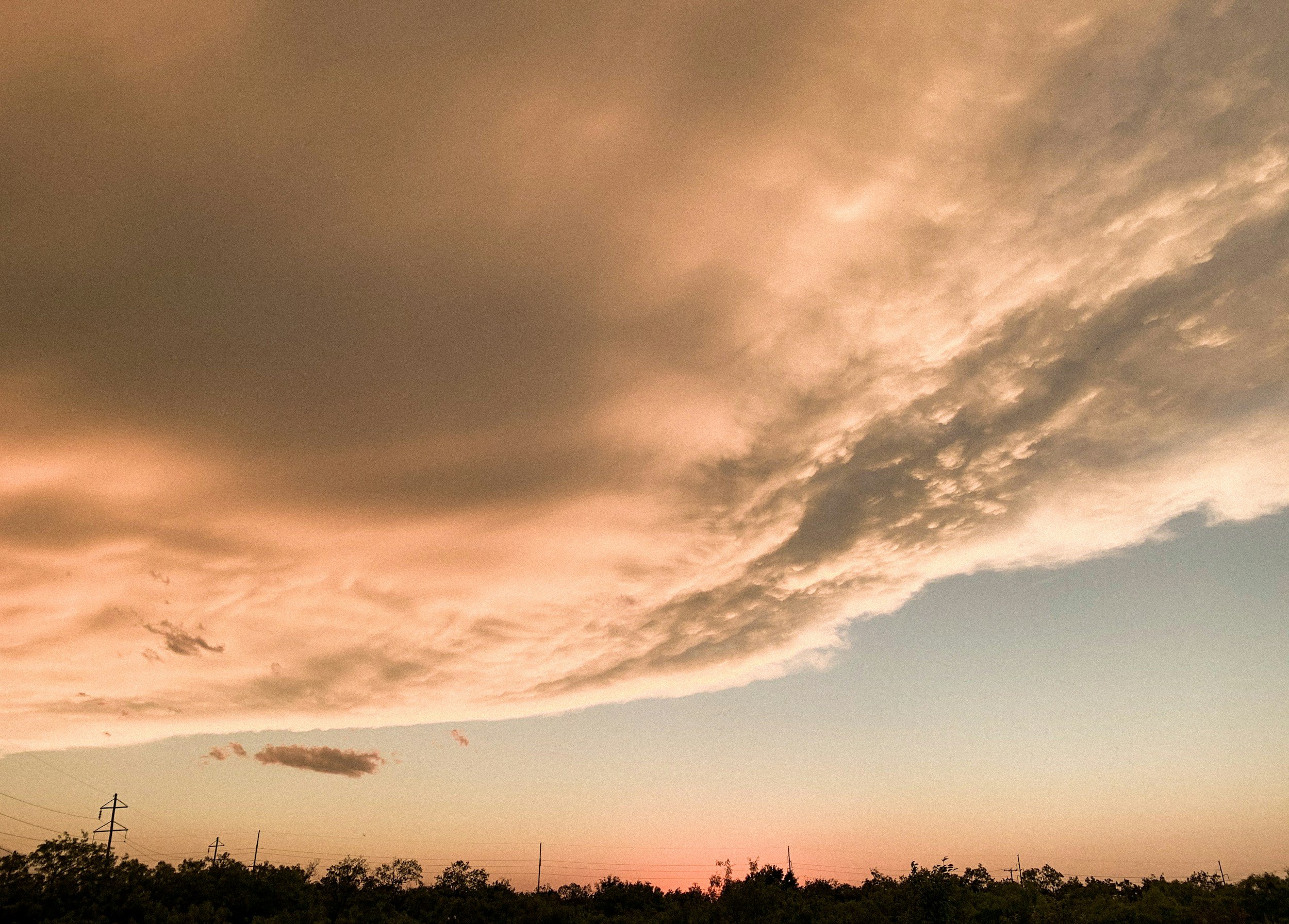 Sky with clouds showing shades of pink and gray, trees silhouette at the bottom, power lines and poles visible.