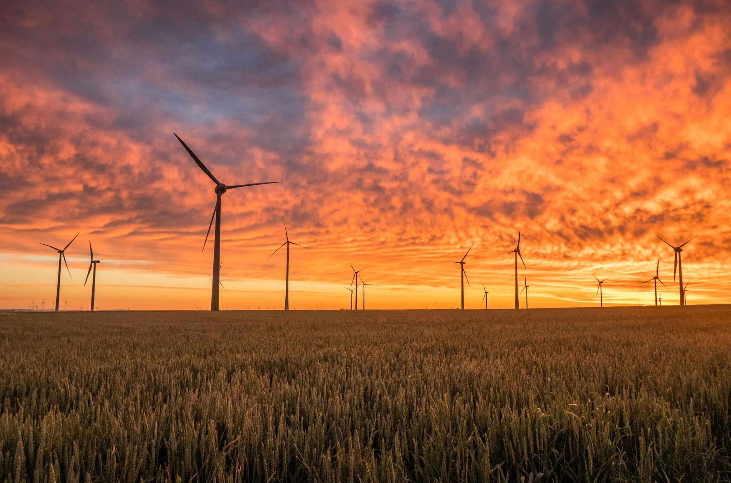 Wind turbines in a field during sunset with a colorful sky of orange and purple clouds.