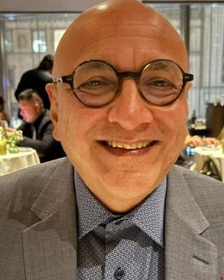 Smiling man with glasses and a gray suit in a restaurant setting.