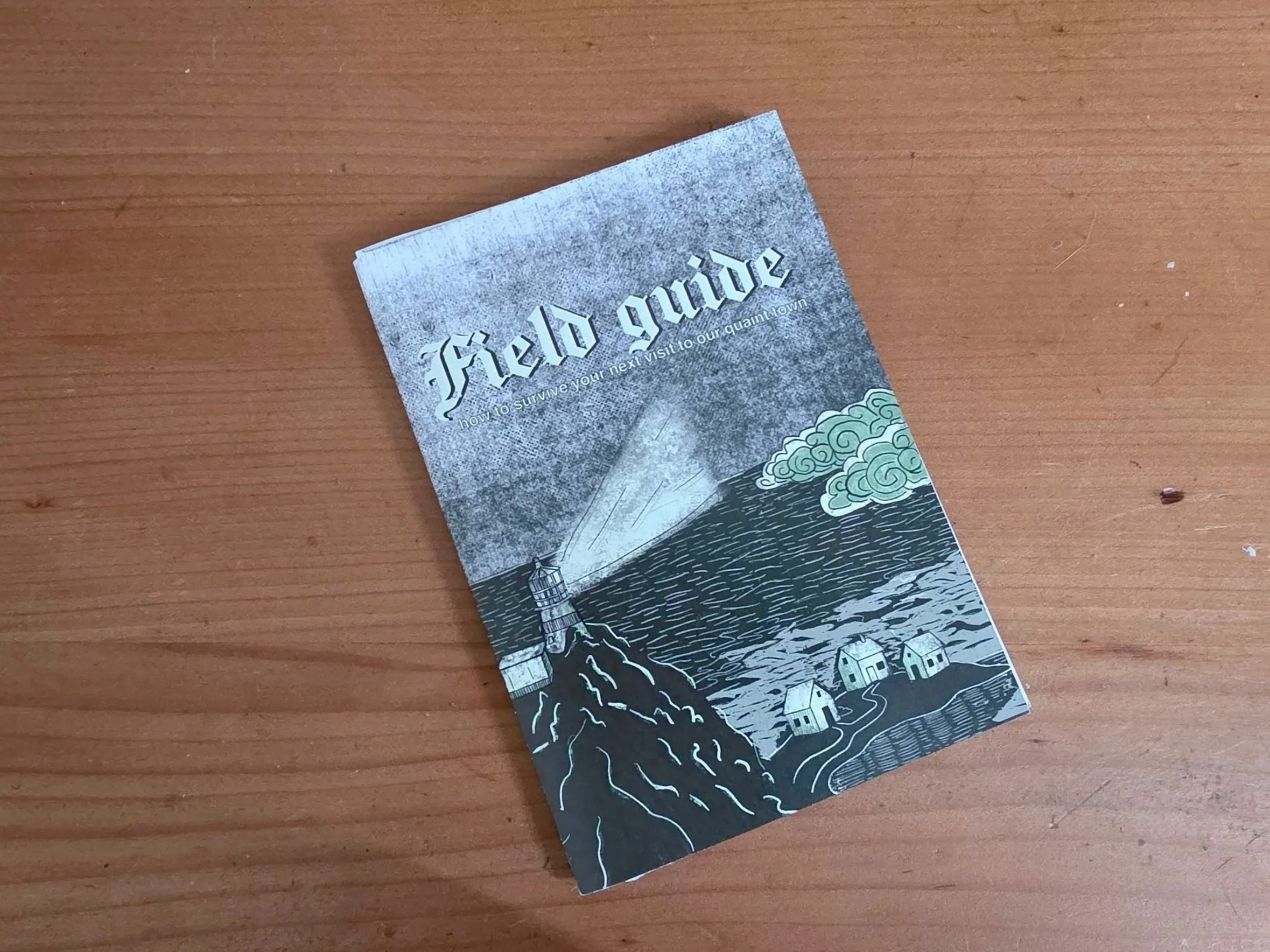 A pamphlet titled 'Fáilte' with an illustration of a lighthouse, waves, clouds, and houses on a wooden surface.