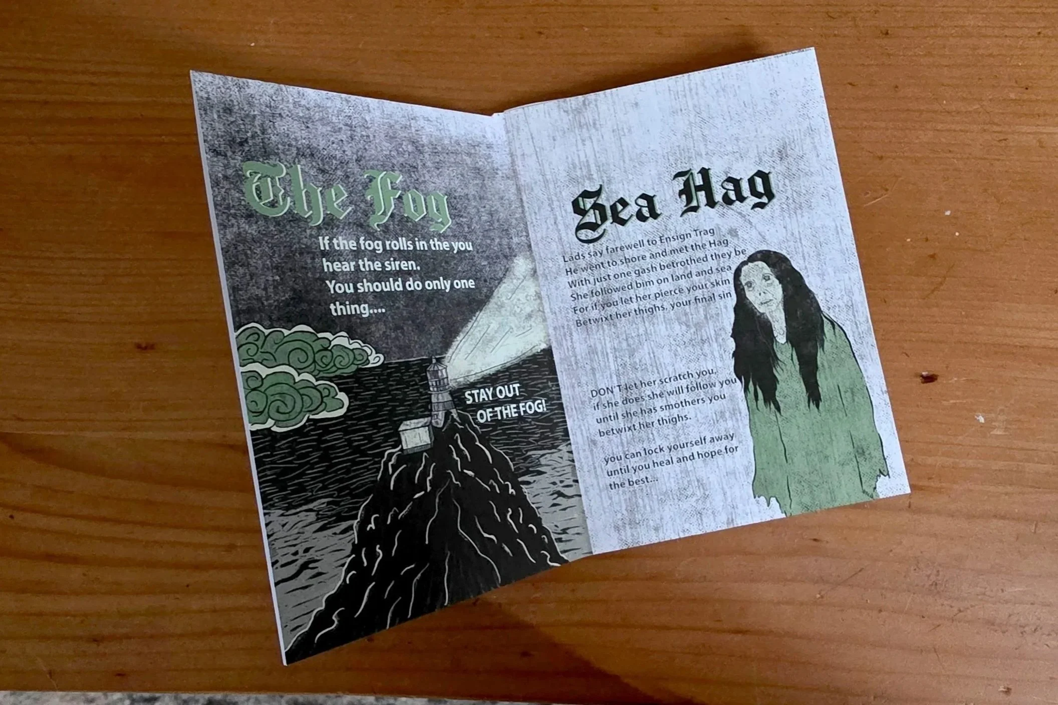 A folded leaflet on a wooden surface features a poem titled "The Fog" and an illustration of a woman with long dark hair, wearing a green dress.