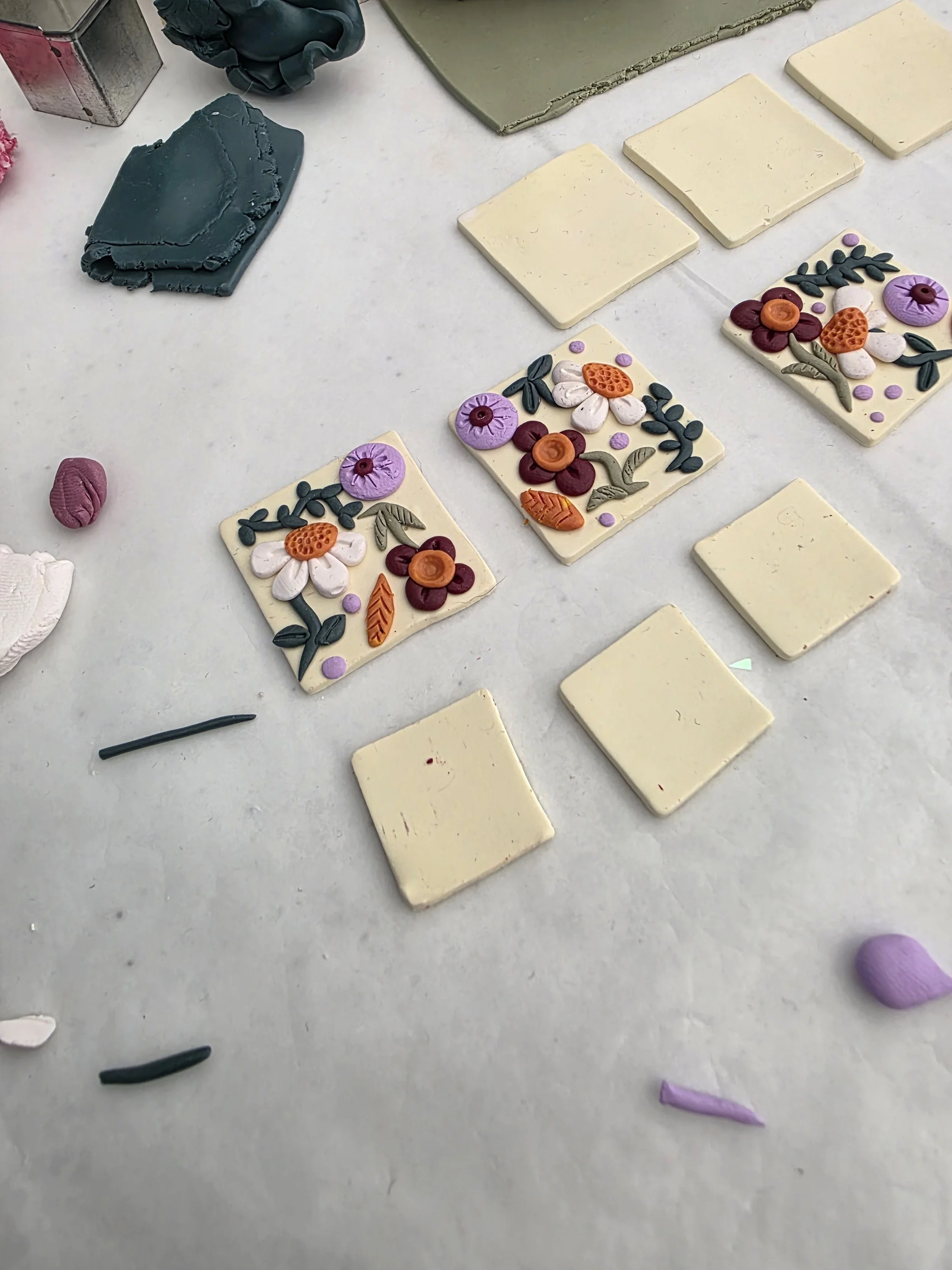 Colorful clay flower and leaf decorations on white tiles and a white surface.