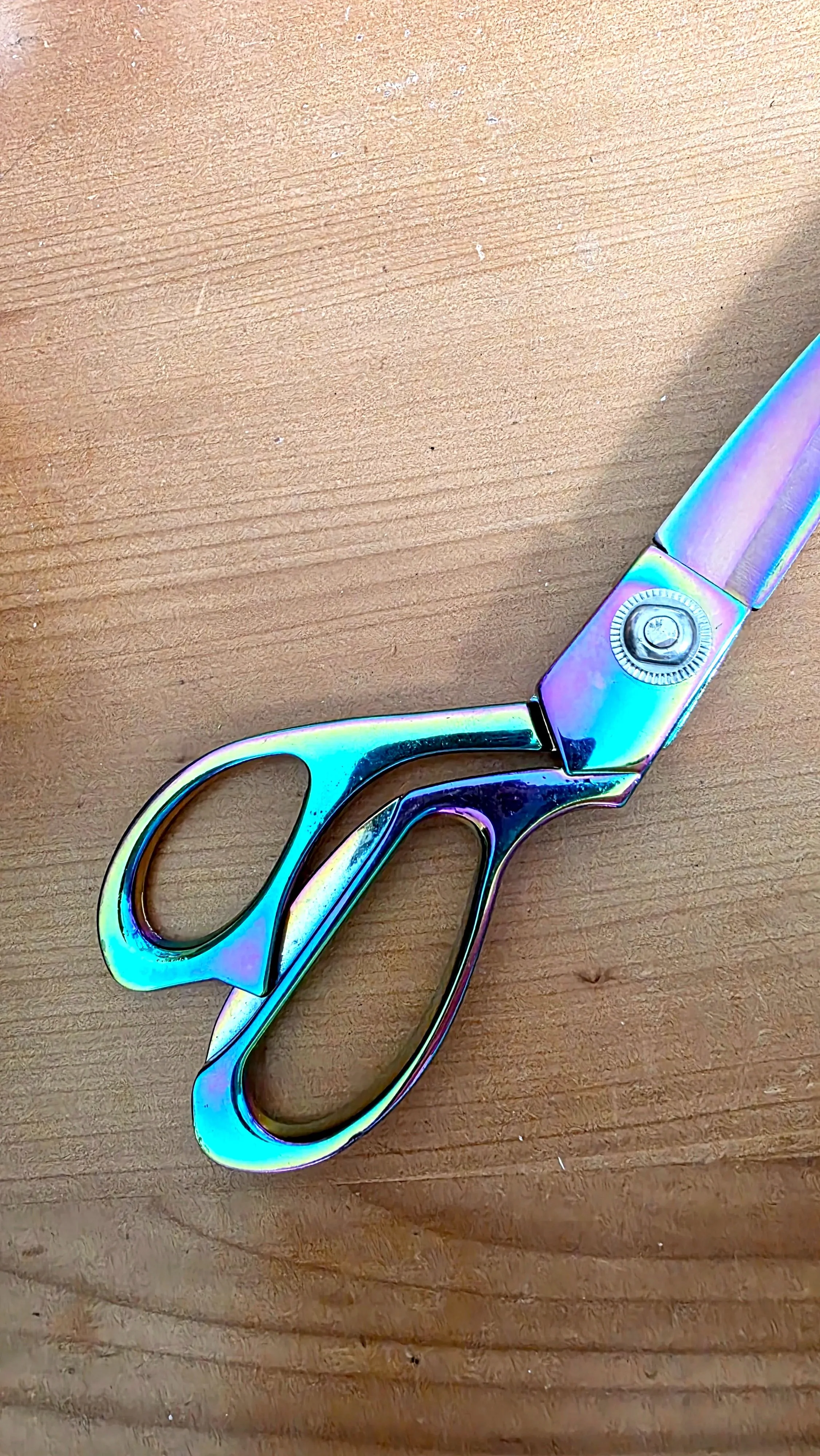 A pair of scissors with a metallic, iridescent finish resting on a wooden surface.