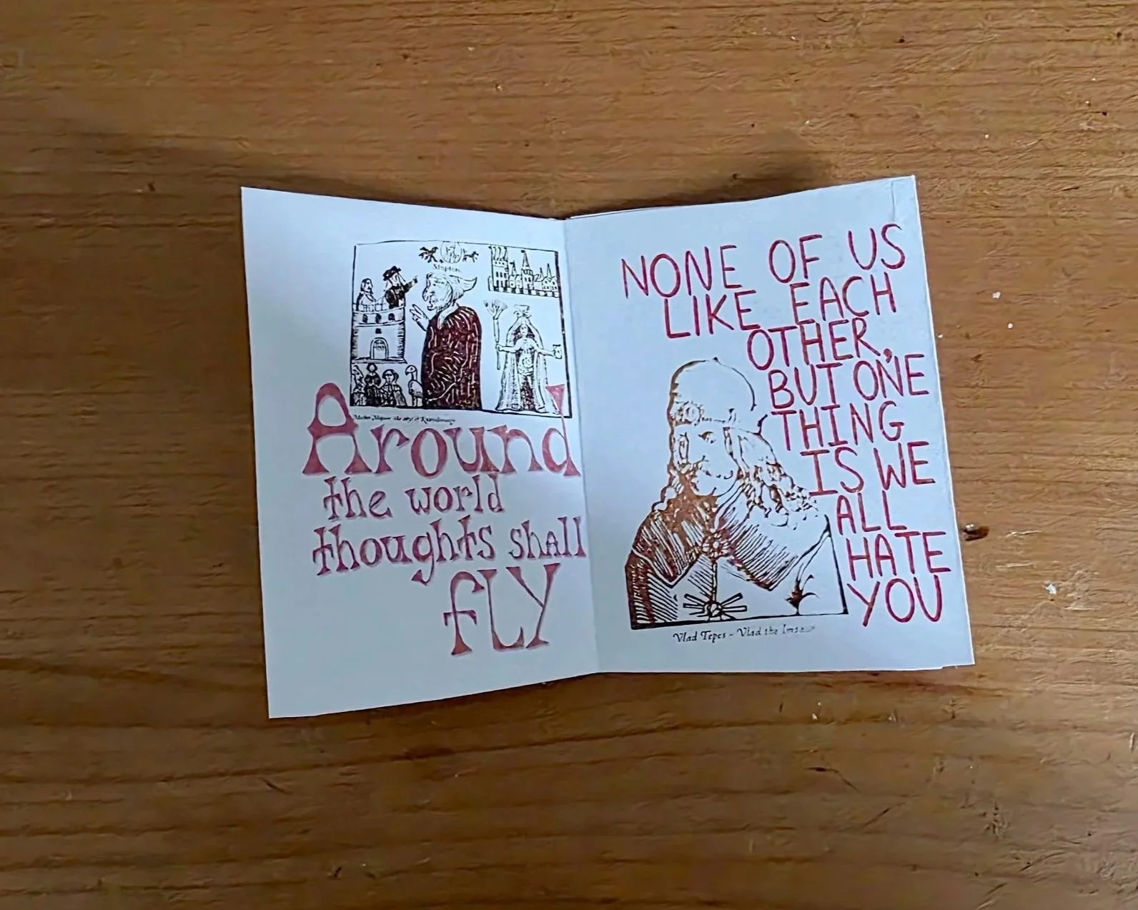 A handwritten note with illustrations. One side has a drawing of a person in historical attire, along with the words "Around the world thoughts shall fly." The other side has a quote: "None of us like each other, but one thing is we all hate you," accompanied by a sketch of a person with long hair.