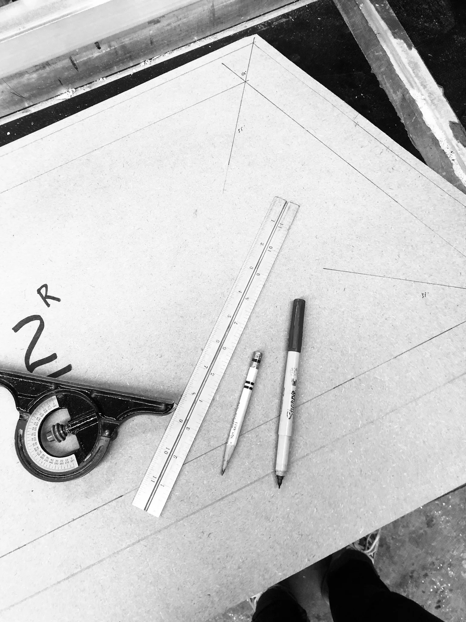 A worktable with drawing tools including a ruler, two markers, a protractor, and a drafting compass, with pencil sketches and measurements on paper.