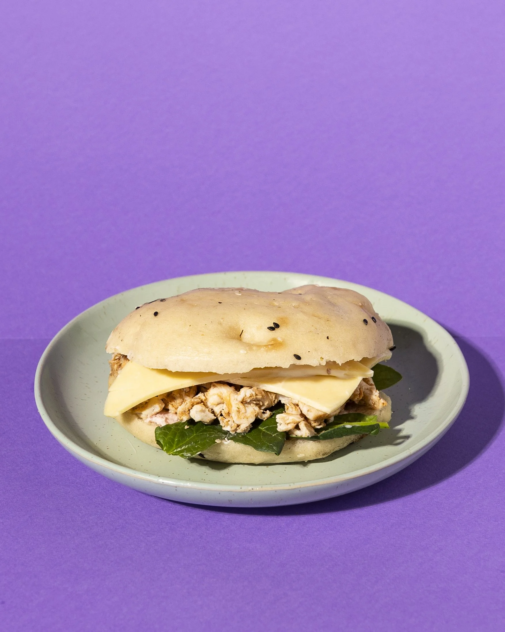 Sandwich with chicken, swiss cheese, cranberry cream cheese, spinach, on a light blue plate against a purple background.