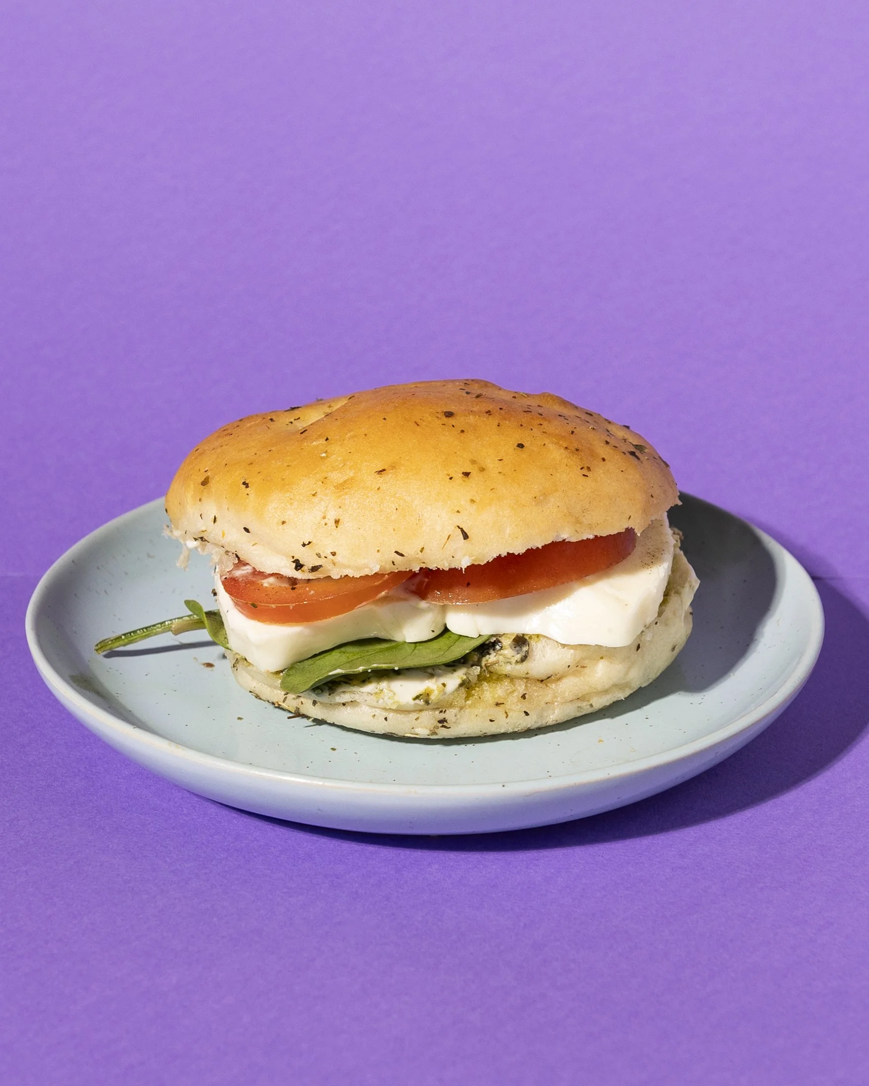 Sandwich with tomato, mozzarella, and spinach with Basil Pesto and aioli, on a blue plate against a purple background.