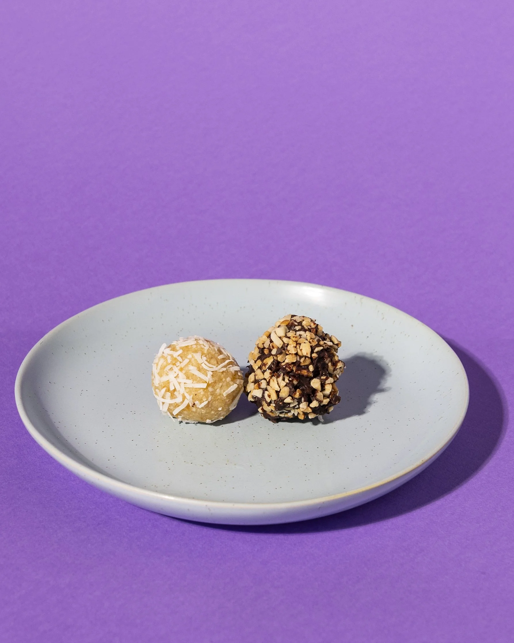 Two chocolate and vanilla truffles on a white plate against a purple background. Made fresh and served best with espresso coffee