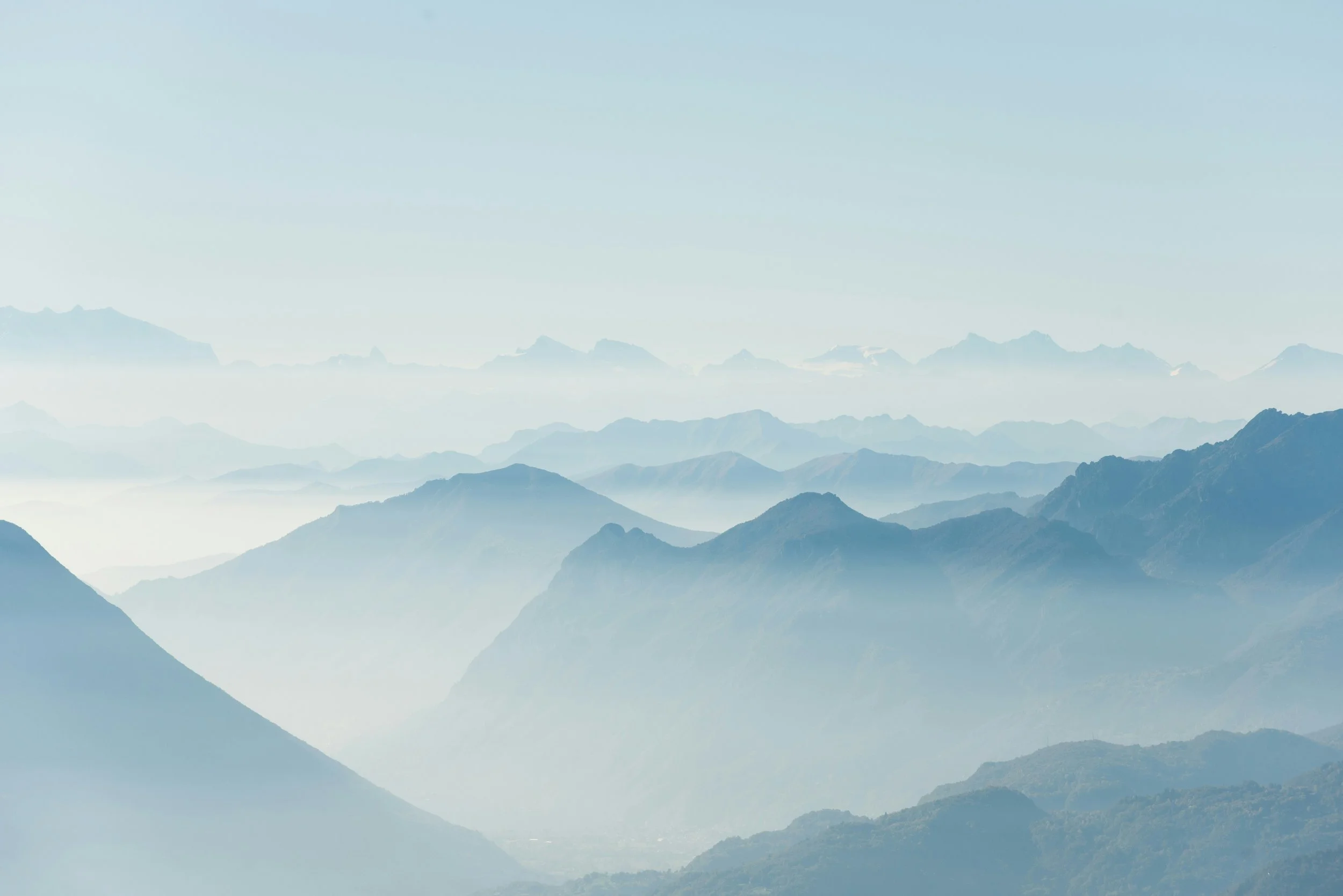 A mountain range with multiple peaks, partially covered in mist or clouds, under a clear sky.