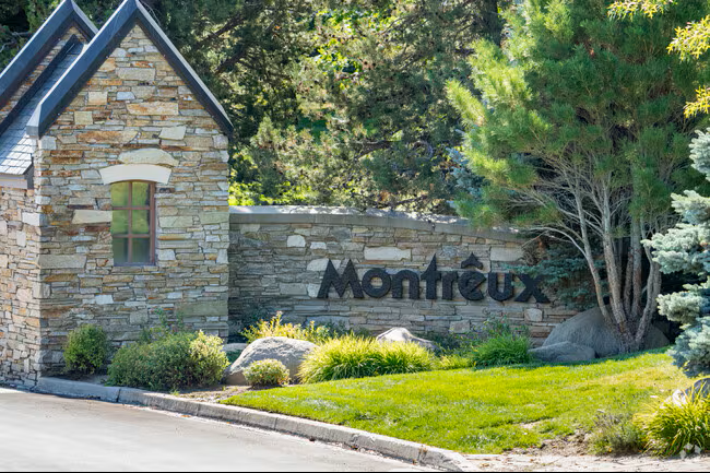 Stone wall with black lettering spelling 'Montreux' in front of a building and surrounded by green trees and shrubs.