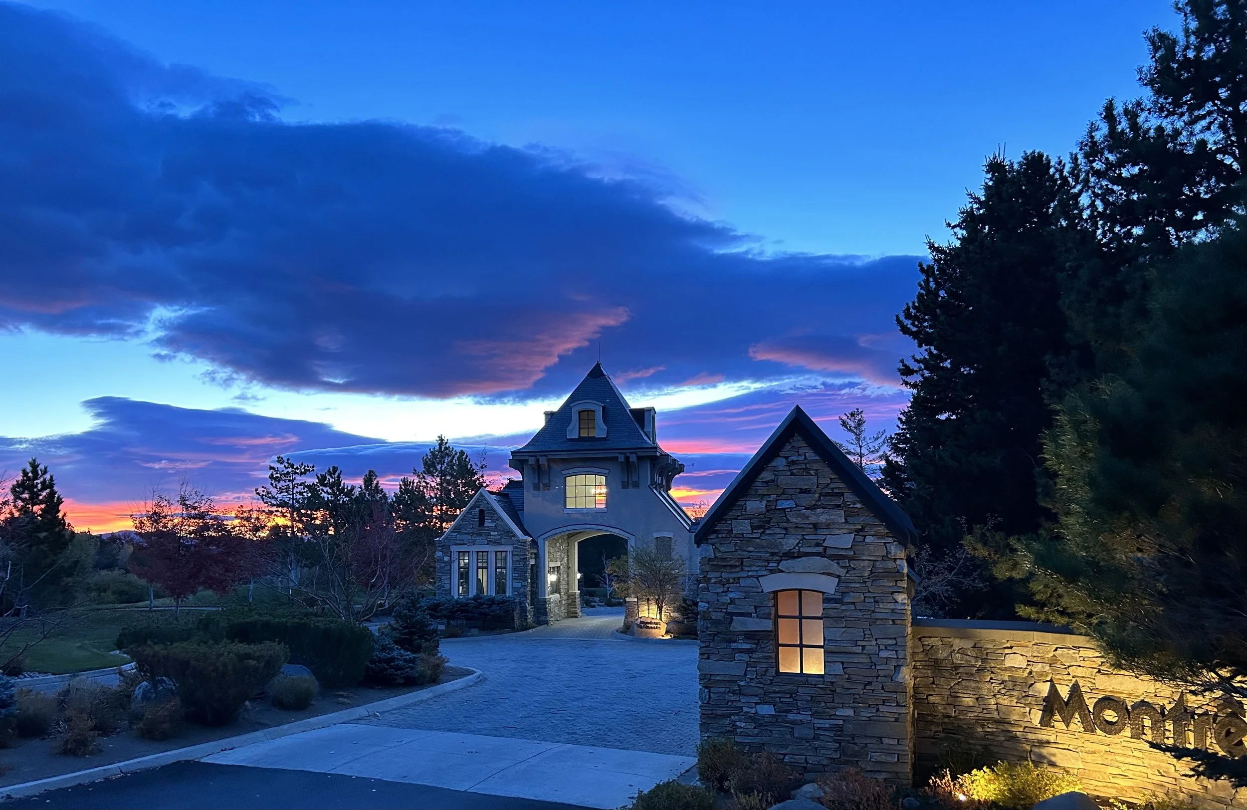 Montreux gatehouse illuminated at dusk, surrounded by trees and a landscaped driveway.