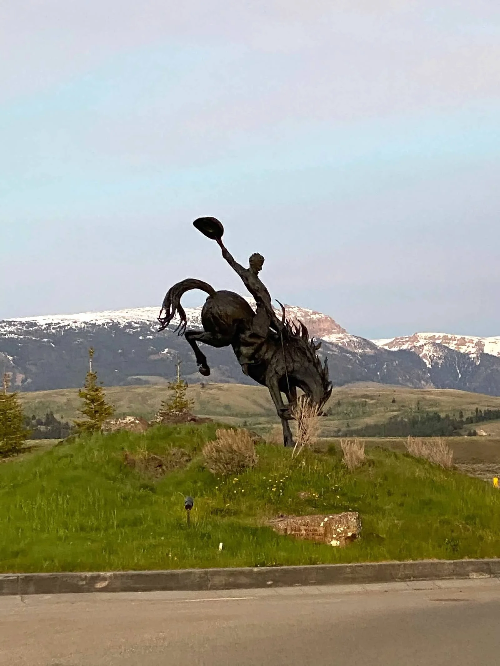 Bronze bucking horse and rider statue with snow-capped mountains in the background