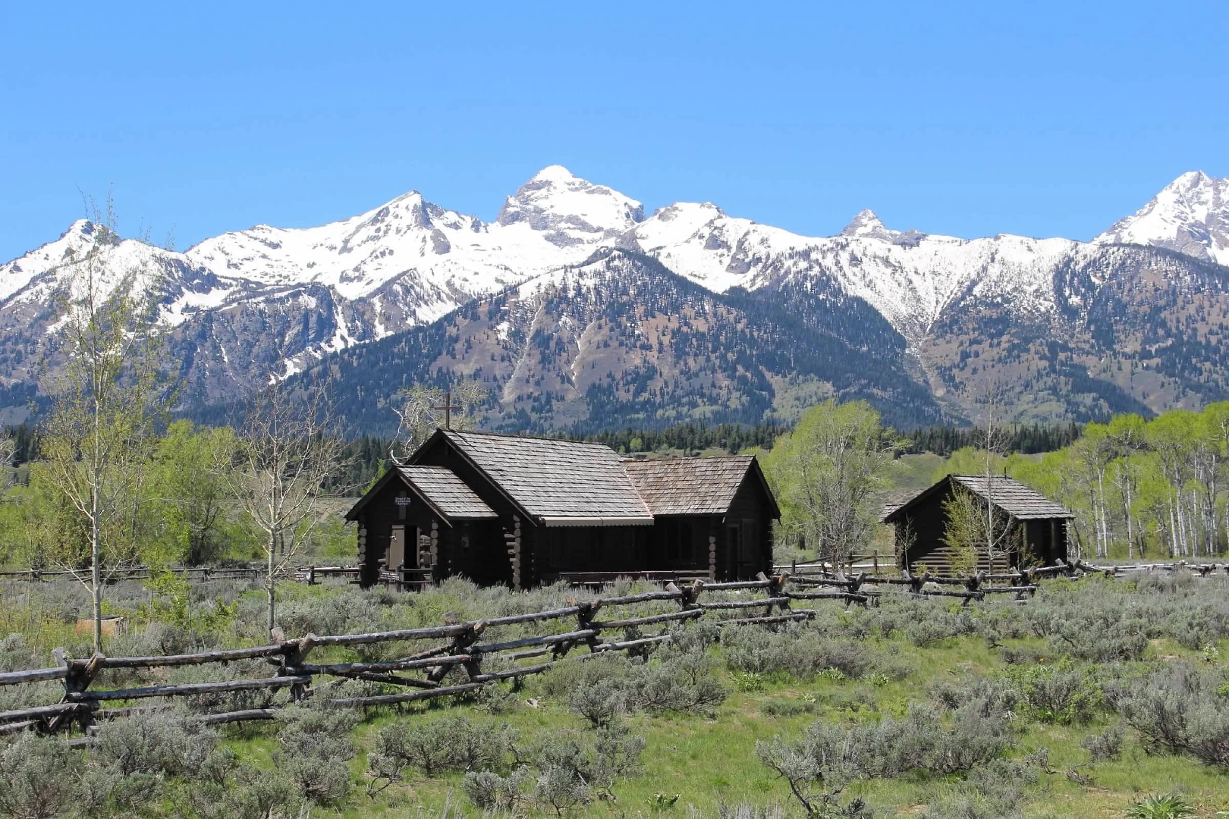 Snow-capped Teton mountains behind a rustic log cabin in Grand Teton National Park