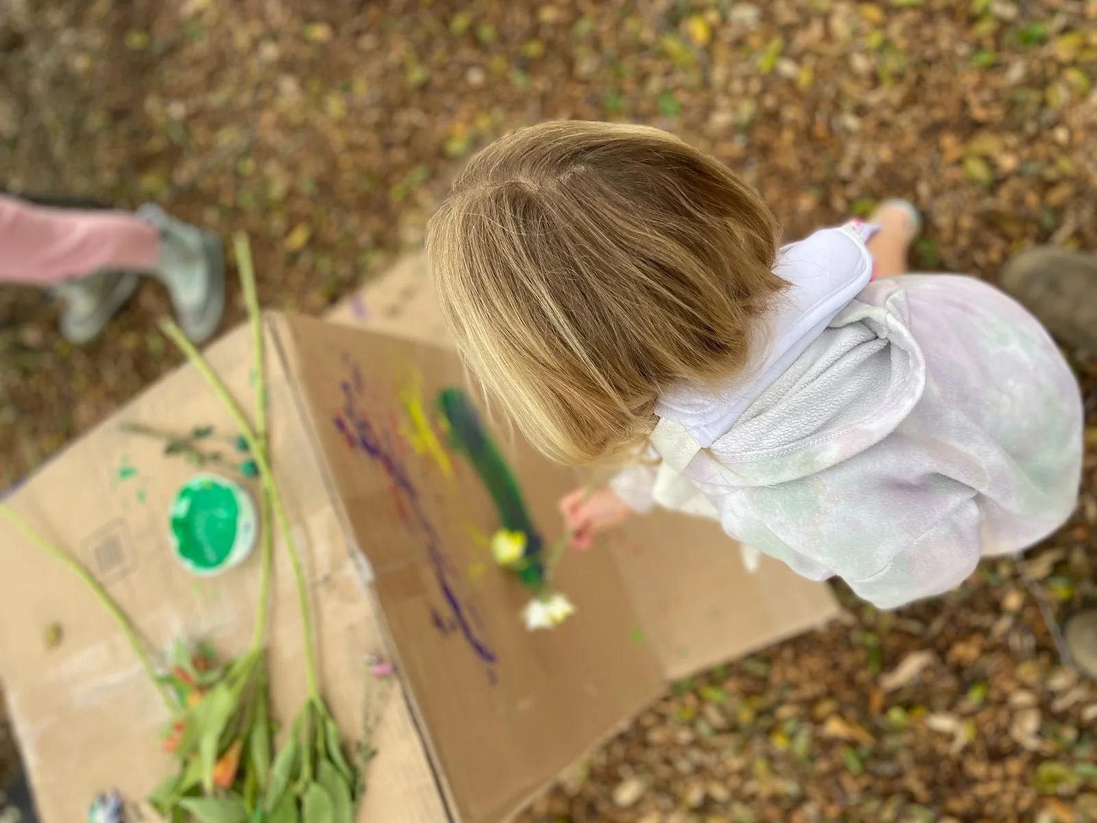 A child painting on cardboard outdoors with flowers and natural materials at Big Tree Little Preschool in Vista, California