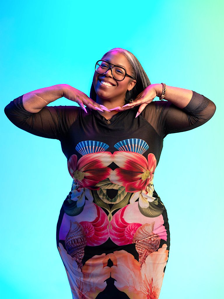 Ty Alexander with glasses posing with hands under chin against a colorful gradient background.