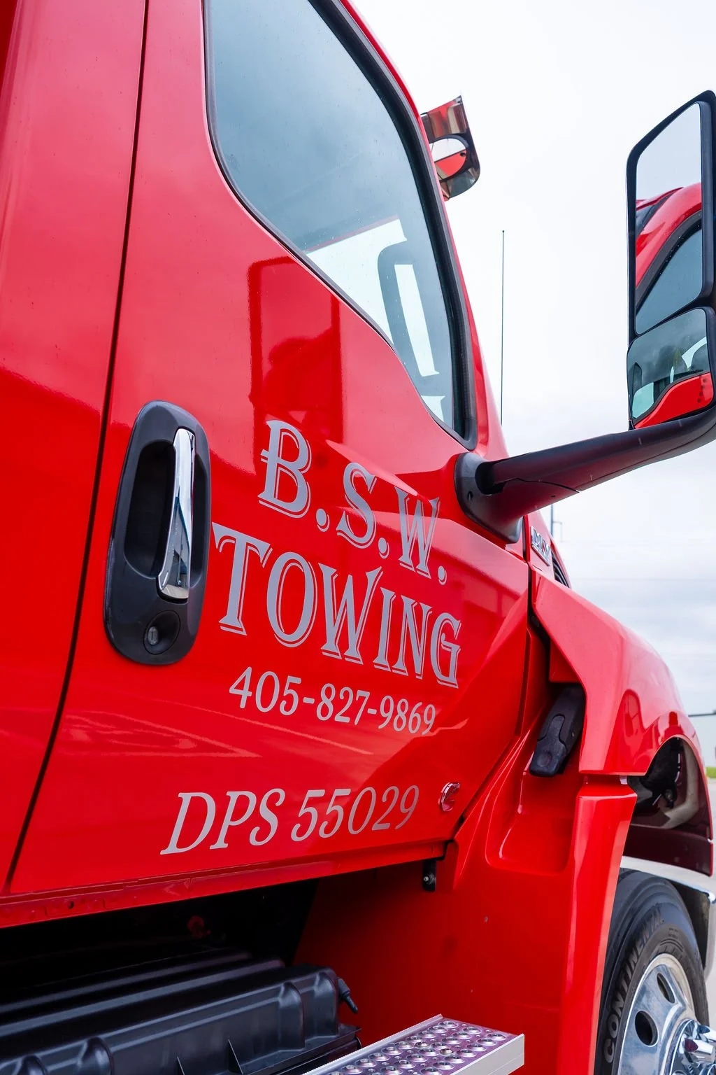 Close-up of a red towing truck with the company's name, phone number, and identification number displayed on the door.