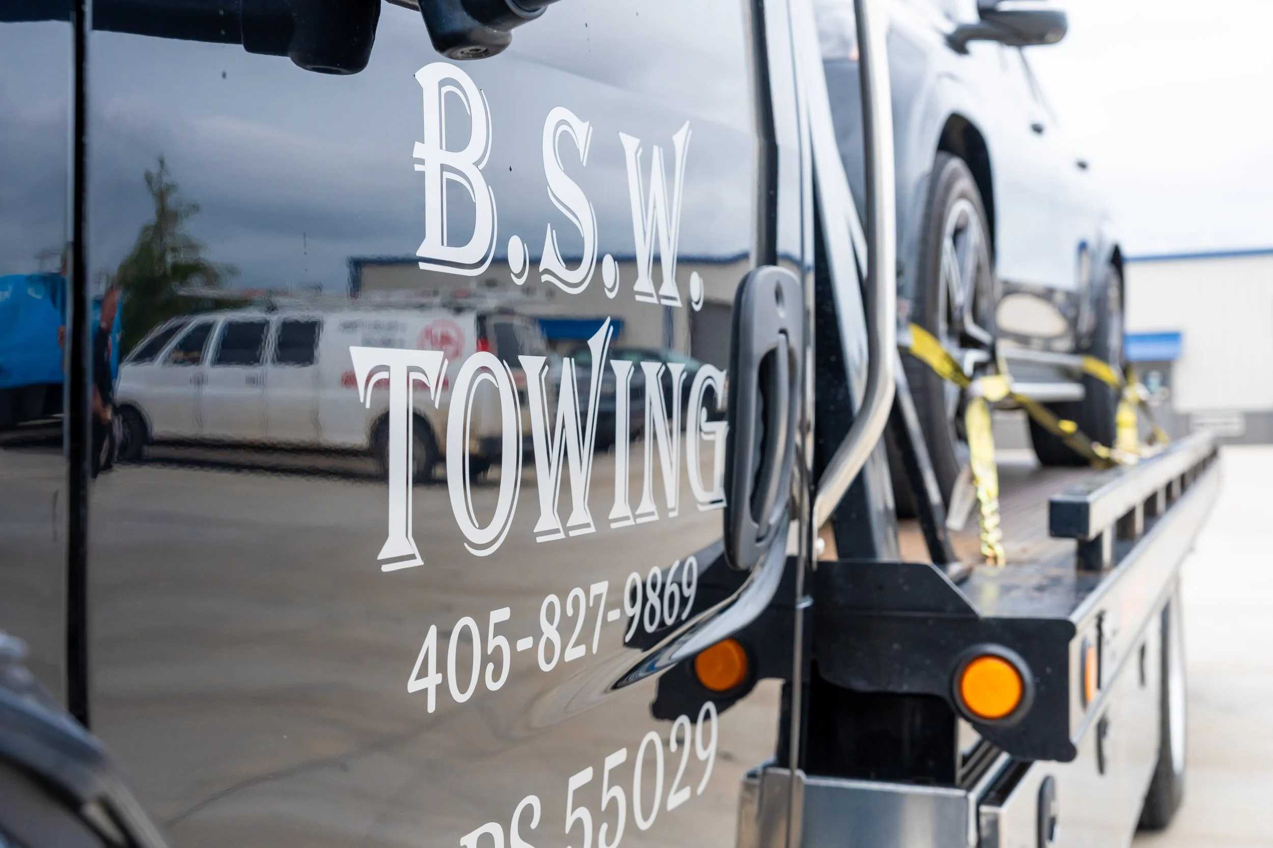 Close-up of the side of a black truck with white lettering that reads 'B.S.W,' a phone number, and other text.
