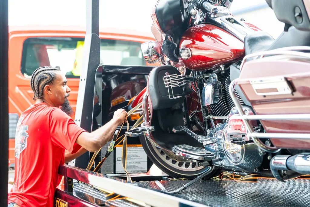 A man with braided hair and a beard loading a red motorcycle onto a transport truck.