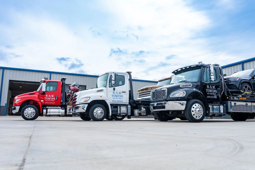 Three tow trucks parked side by side outside a building, with clear sky and some clouds overhead.