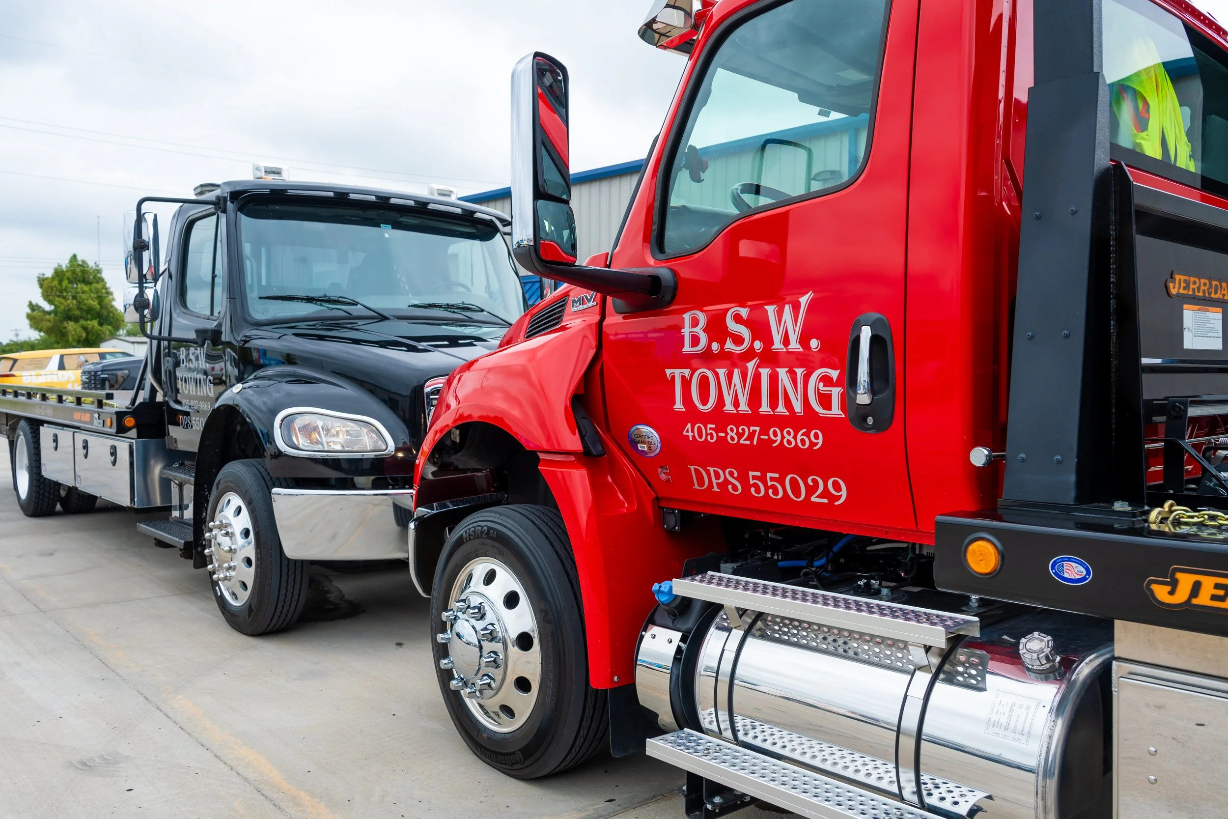 A row of tow trucks parked on a parking lot. The trucks are black and red with company name B.S.W. Towing and contact number 405-827-9869 on the doors. The trucks have large mirrors and chrome wheels.
