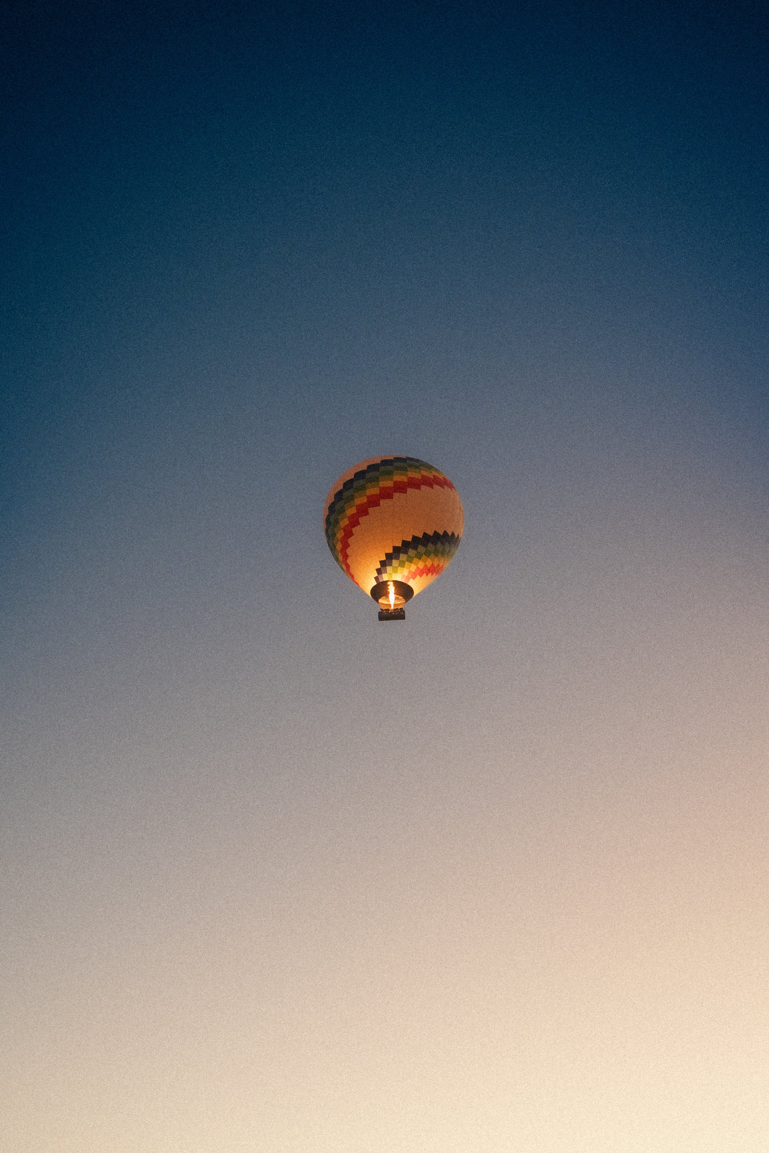 A colorful hot air balloon flying in the evening sky with a gradient of blue to orange.