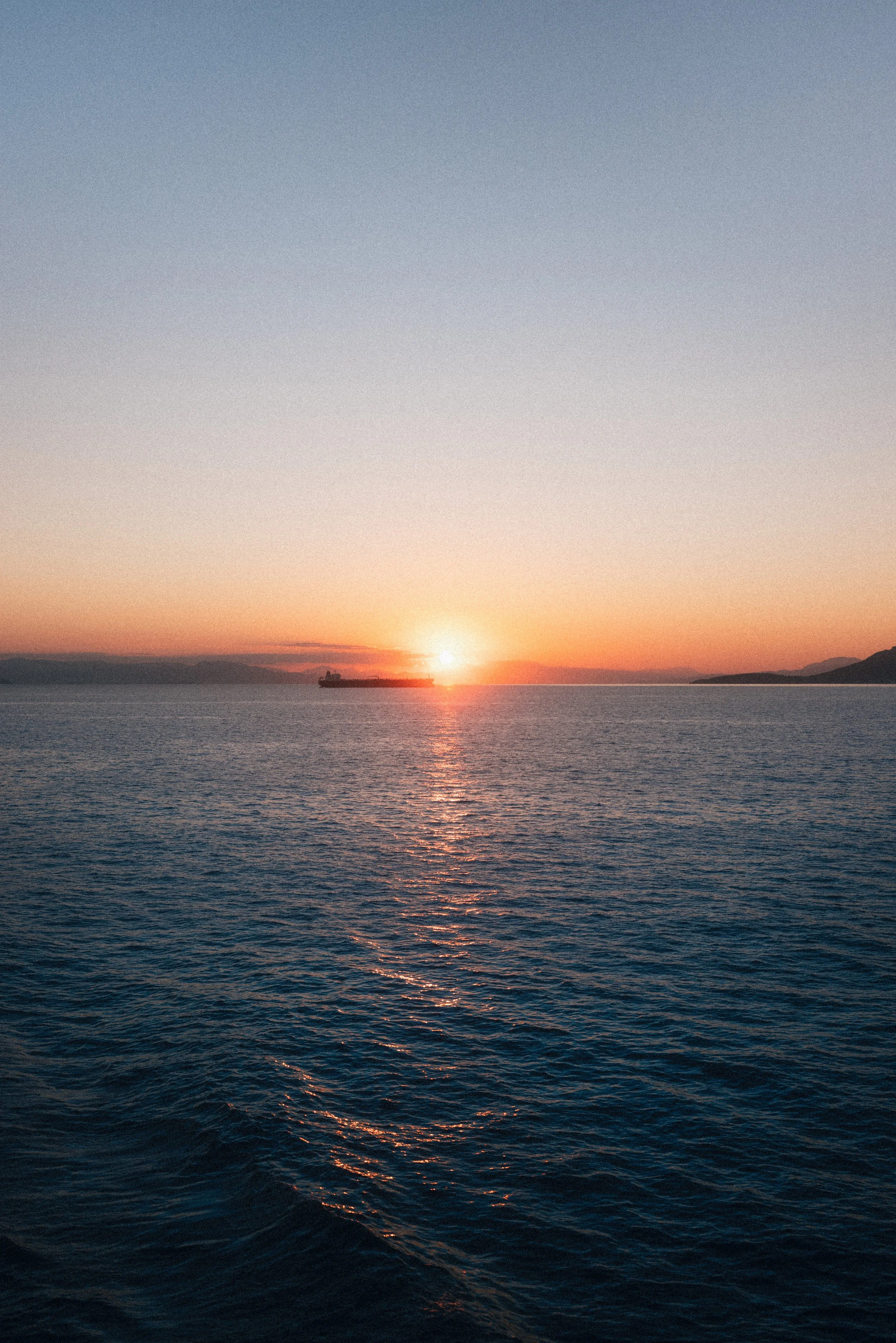 A ship sailing across the ocean during sunset with mountains in the background.