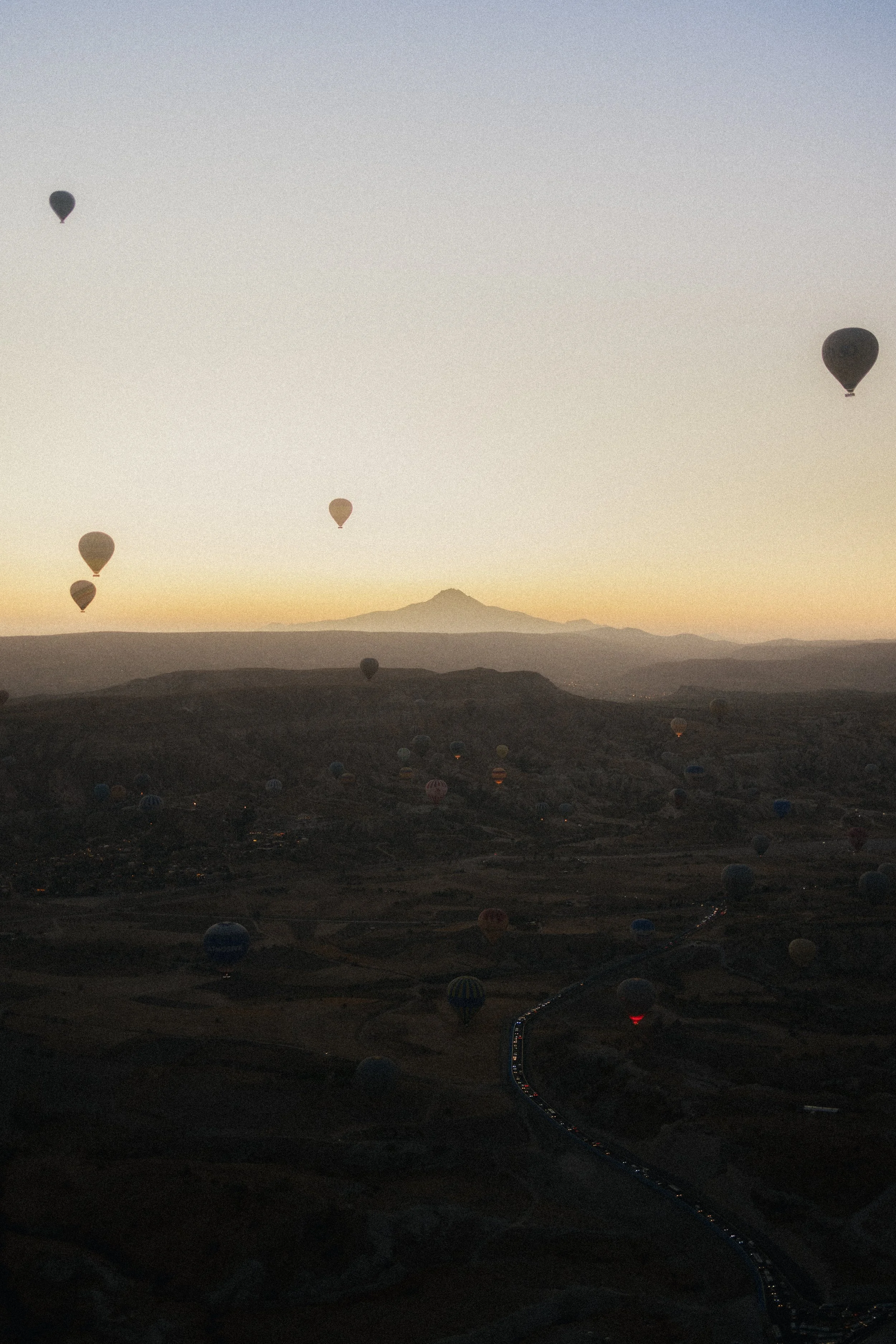 Hot air balloons floating over a mountainous landscape at dawn or dusk with a clear sky.