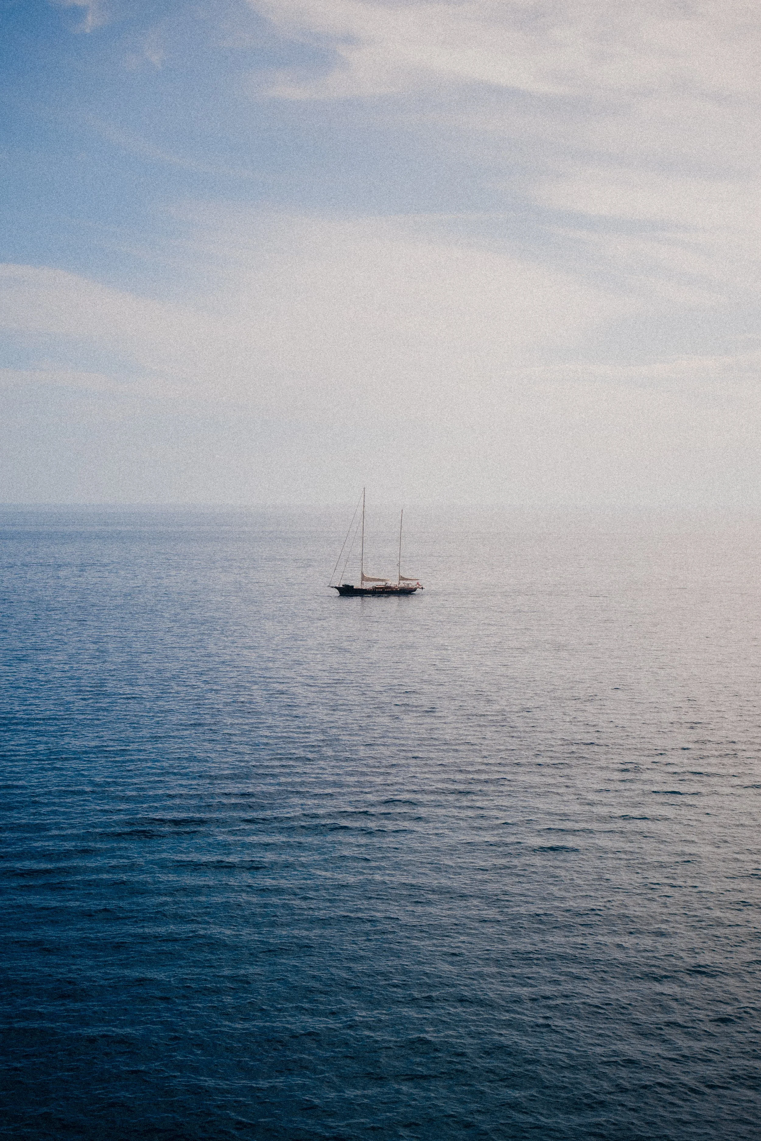 A sailboat floating on calm water with a clear sky in the background.