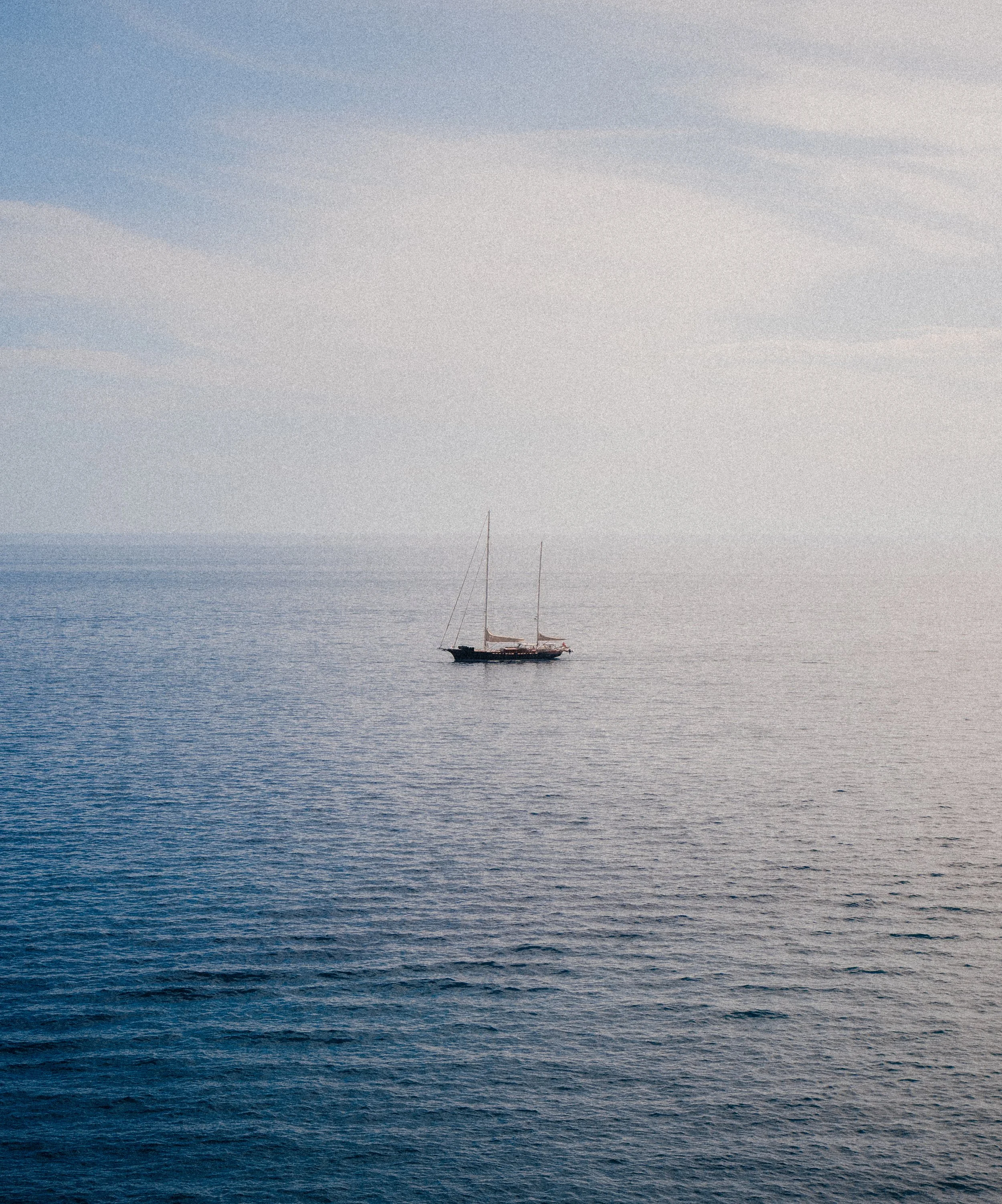 Sailboat sailing on calm ocean waters under a partly cloudy sky.