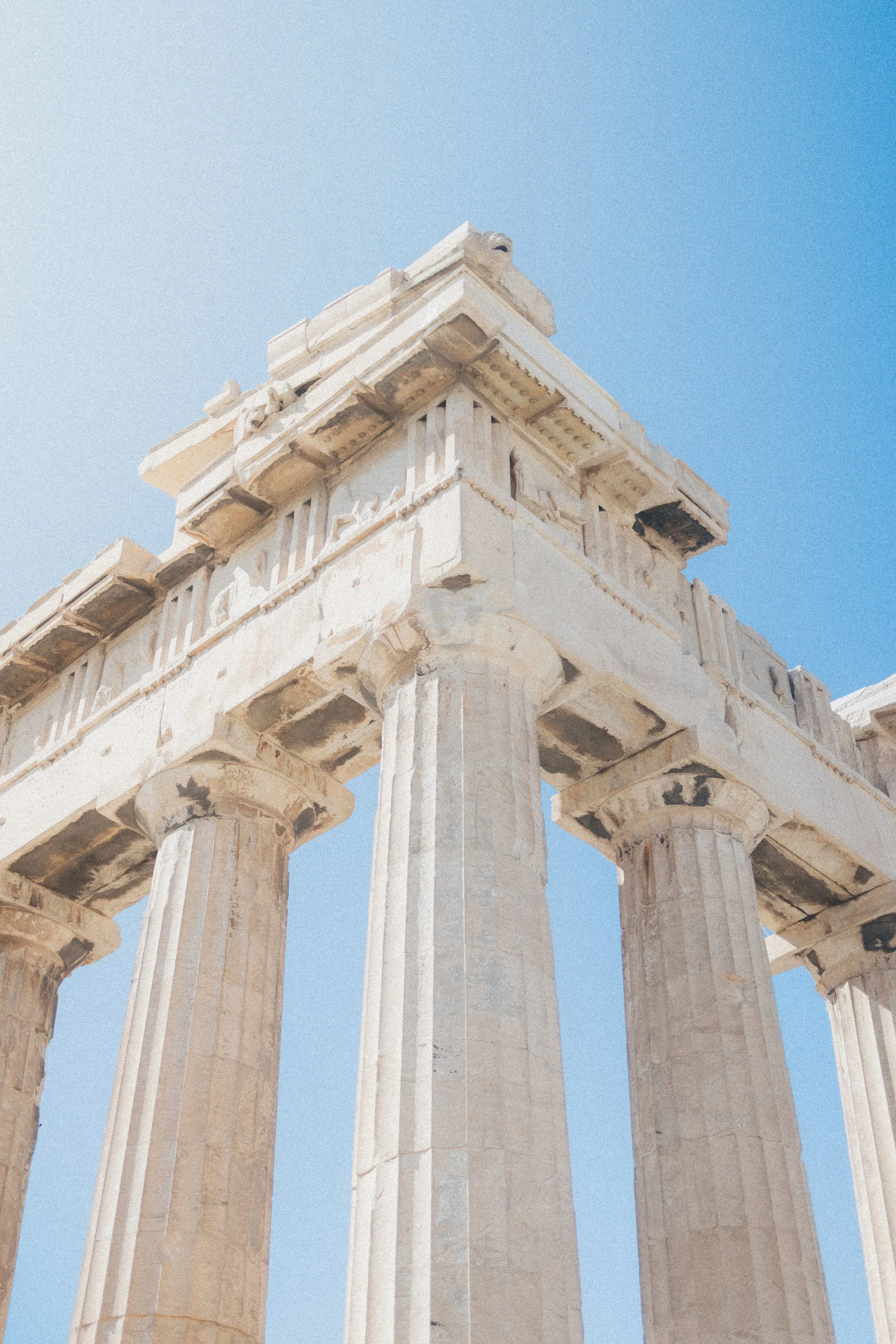 Close-up view of the top section of ancient Greek marble columns with a clear blue sky in the background.