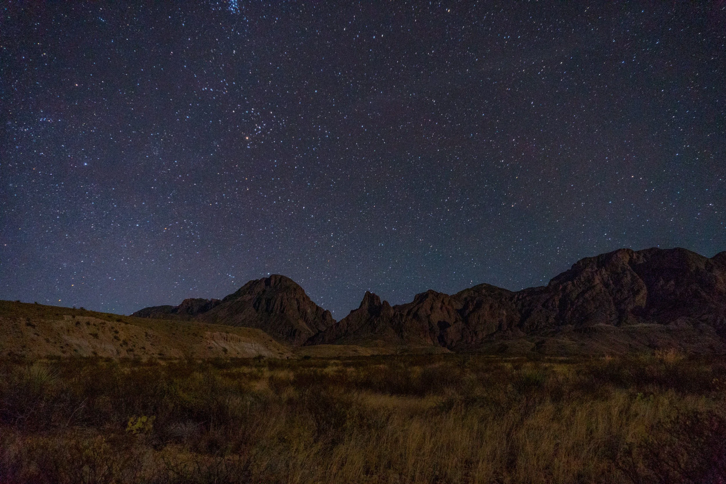 Nighttime landscape of mountains with a starry sky overhead.