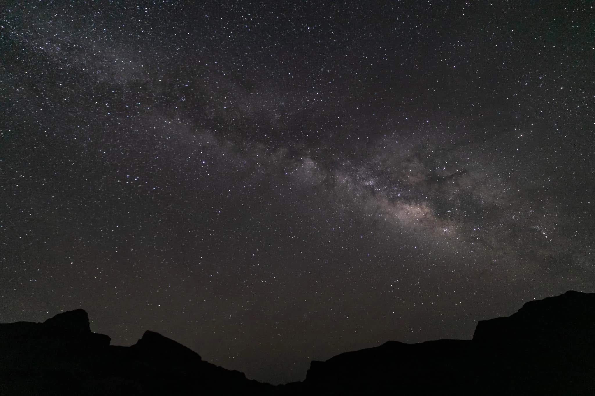 Night sky filled with stars and the Milky Way galaxy above a silhouette of mountains or rocks.