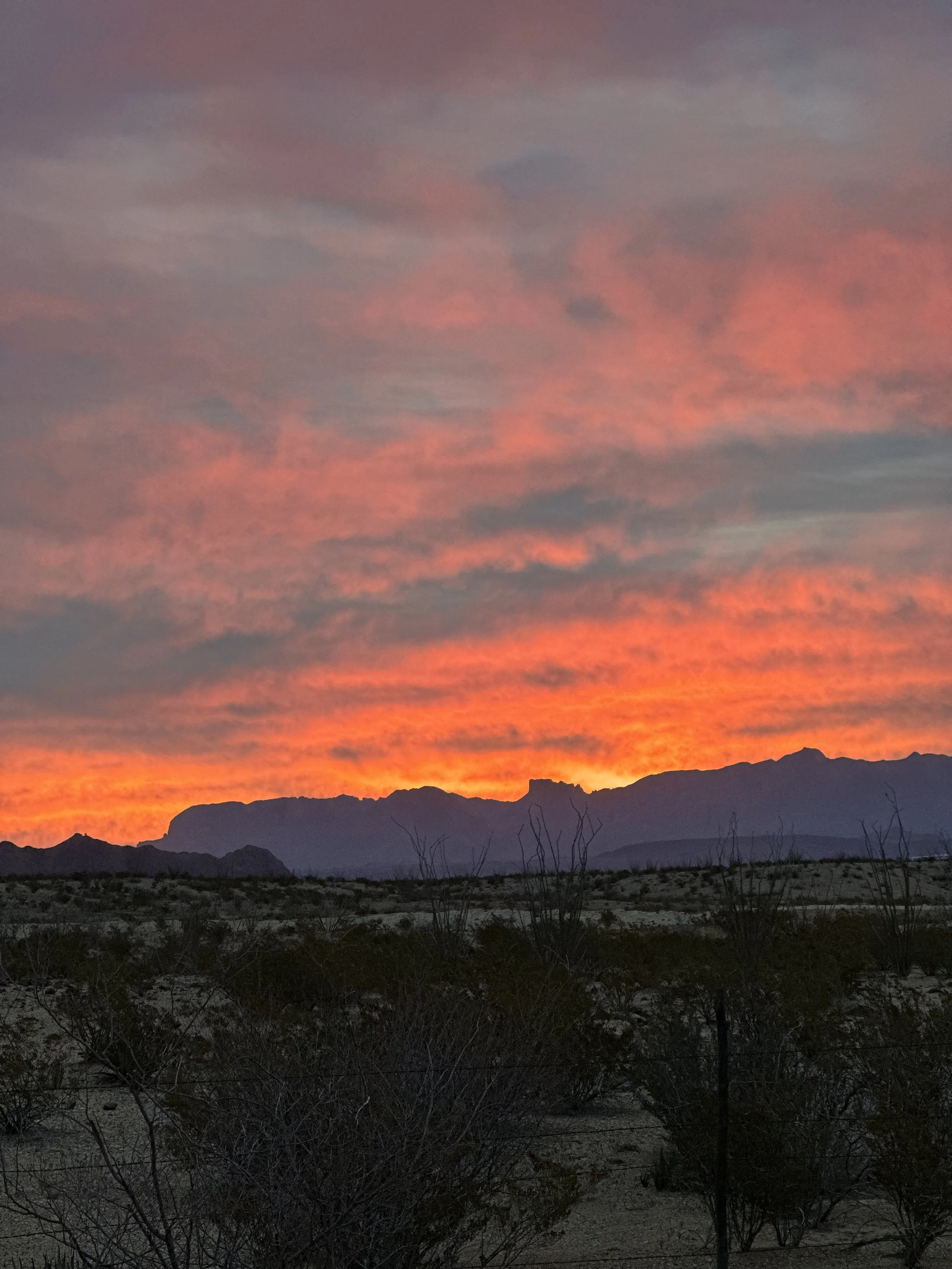Desert landscape at sunset with mountain silhouettes and colorful sky in shades of pink, orange, and purple.