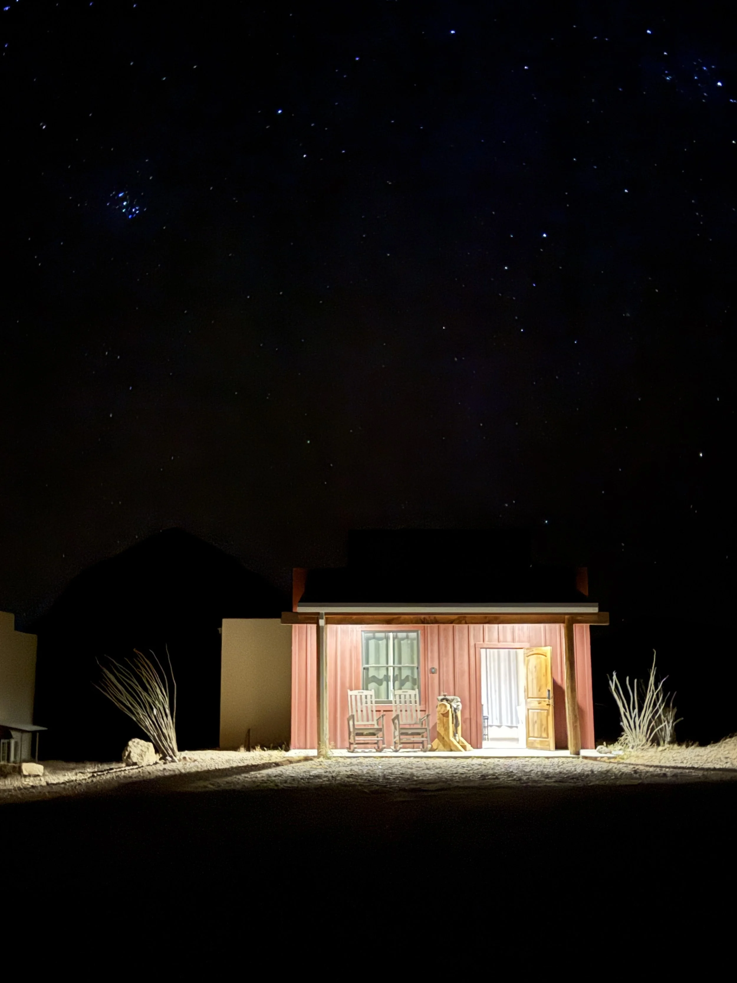 Nighttime view of a house with a porch, illuminated from inside, against a dark sky filled with stars.